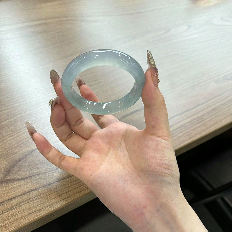 Translucent light blue jade bangle held in palm, showing round shape and glossy finish | DIY Jade
