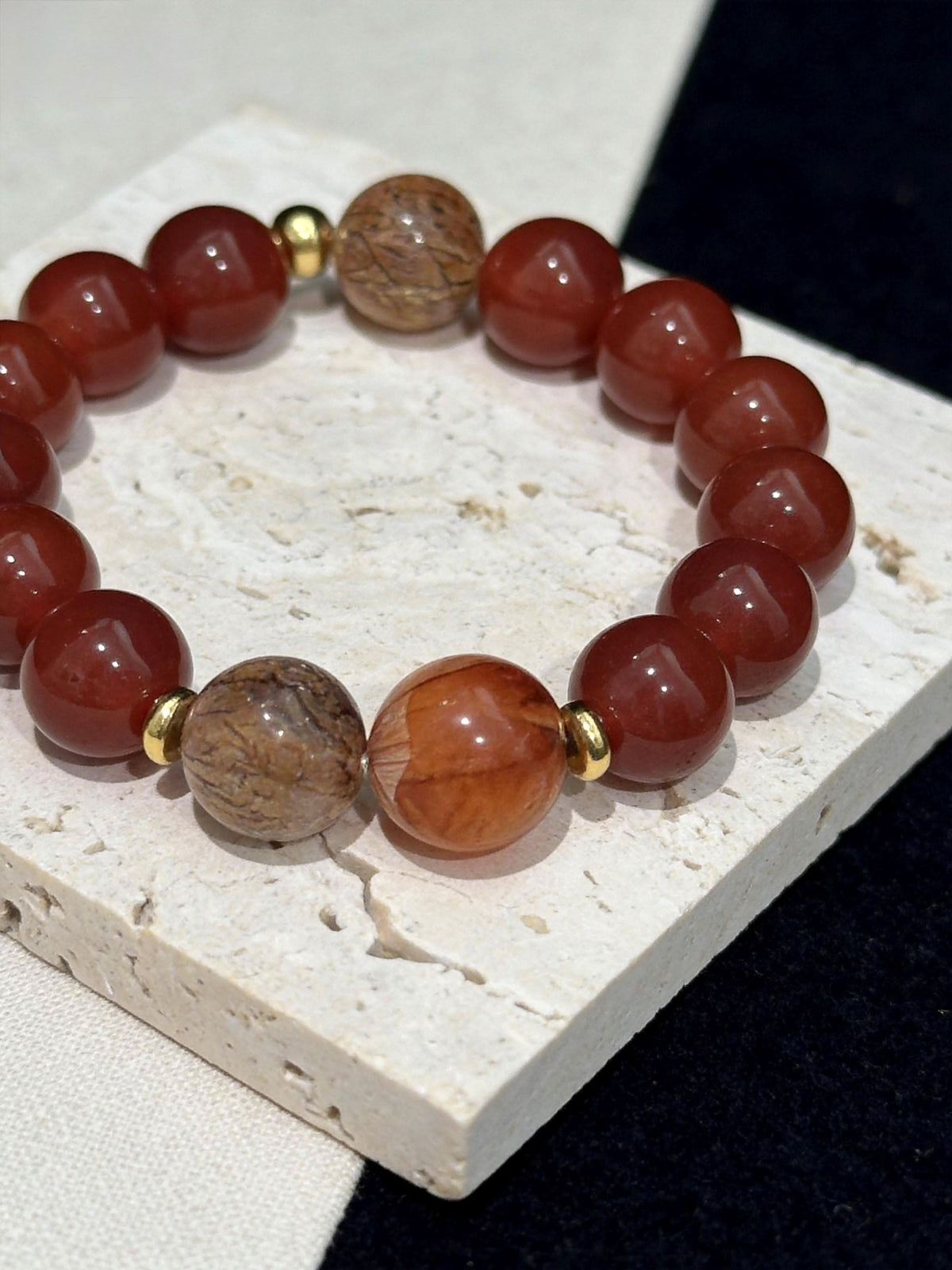 Mixed red‑orange agate round bead human bracelet laid on stone display base | DIY Jade