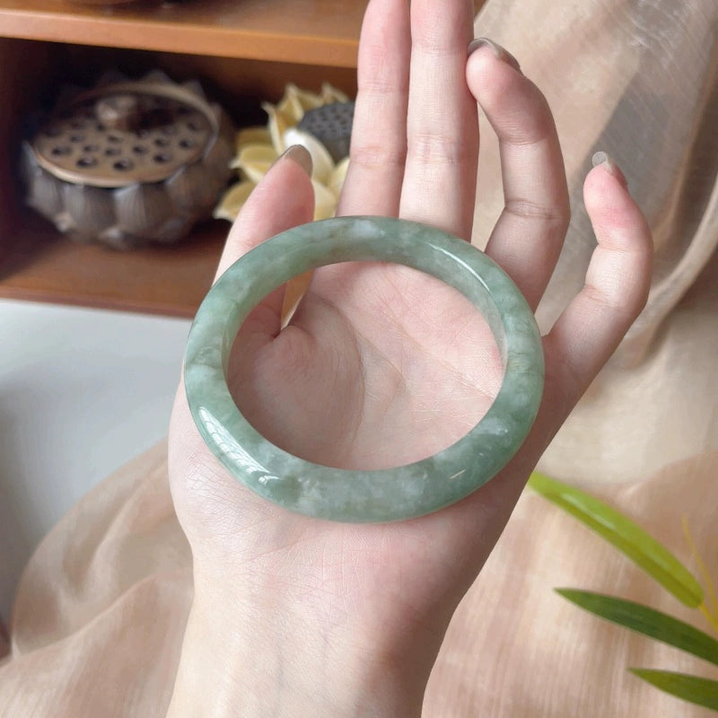 Pale green floating pattern jadeite bangle bracelet, full view held in hand with natural decor | DIY Jade
