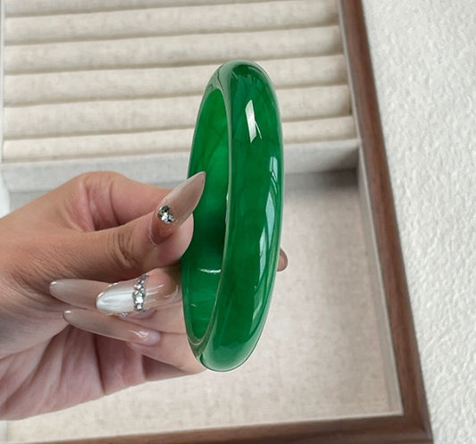 Rich emerald green jade bangle held by hand with manicured nails, glossy finish against jewelry box background | DIY Jade
