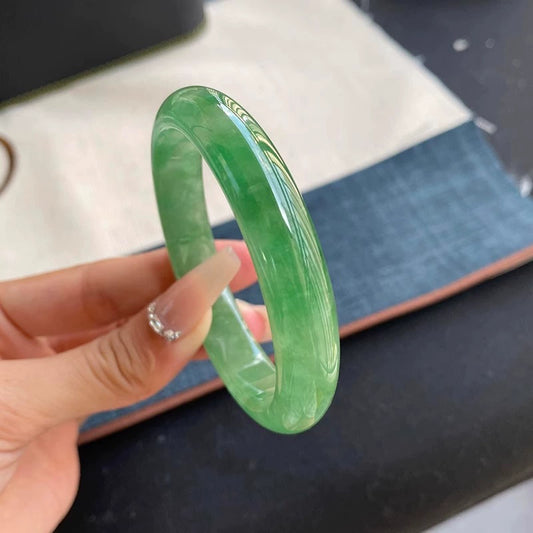 Vibrant green jade bangle held by hand with manicured nails, showing glossy surface and rich color | DIY Jade
